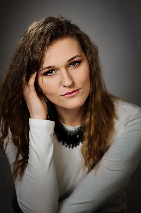 Portret kobiety w białym stroju, opierającej głowę na dłoni, z lekkim uśmiechem