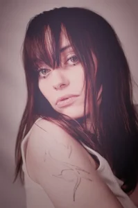 Kobieta z grzywką i tatuażem, patrząca nostalgicznie w dal, w miękkim różowym świetle