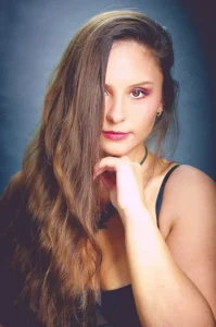 Kobieta z długimi włosami, zmysłowo odsłaniająca twarz, patrząca wprost w obiektyw