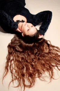 Kobieta ubrana na czarno, leżąca z rozpuszczonymi, falującymi włosami