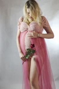 Elegancki portret kobiety w ciąży, ubranej w różową suknię, trzymającej kwiat