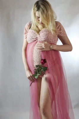 Elegancki portret kobiety w ciąży, ubranej w różową suknię, trzymającej kwiat