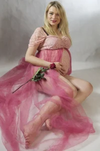 Ciężarna kobieta w różowej sukni, trzymająca różę, w romantycznym świetle