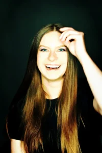 Młoda kobieta w czarnym stroju, śmiejąca się szczerze, poprawiając włosy