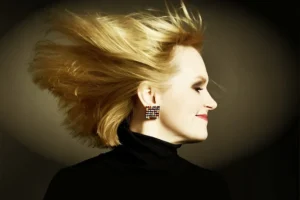 Stylowy portret kobiety w czarnym golfie, jej blond włosy rozwiane przez wiatr, a twarz wyraża spokój i pewność siebie