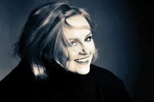 Kobieta w czarnym golfie, jej włosy lekko rozwiane, uśmiecha się radośnie, patrząc na bok