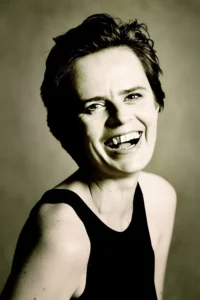 Kobieta w czarnej sukience, śmiejąca się serdecznie, jej twarz pełna radości i spontaniczności