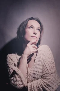 Kobieta w dzianinowym swetrze, z subtelnym makijażem, patrząca w dal w zamyśleniu